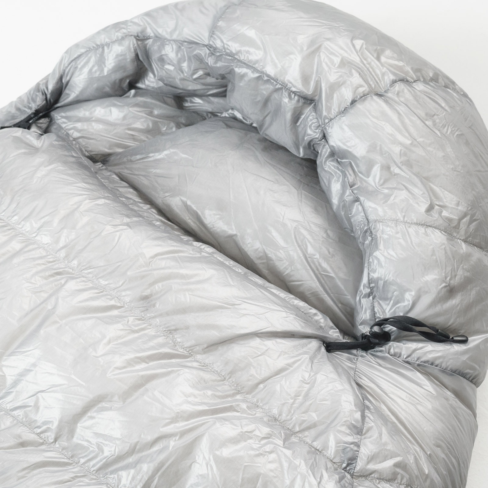 Close-up of a shiny silver puffer sleeping bag with visible stitching and a drawcord.