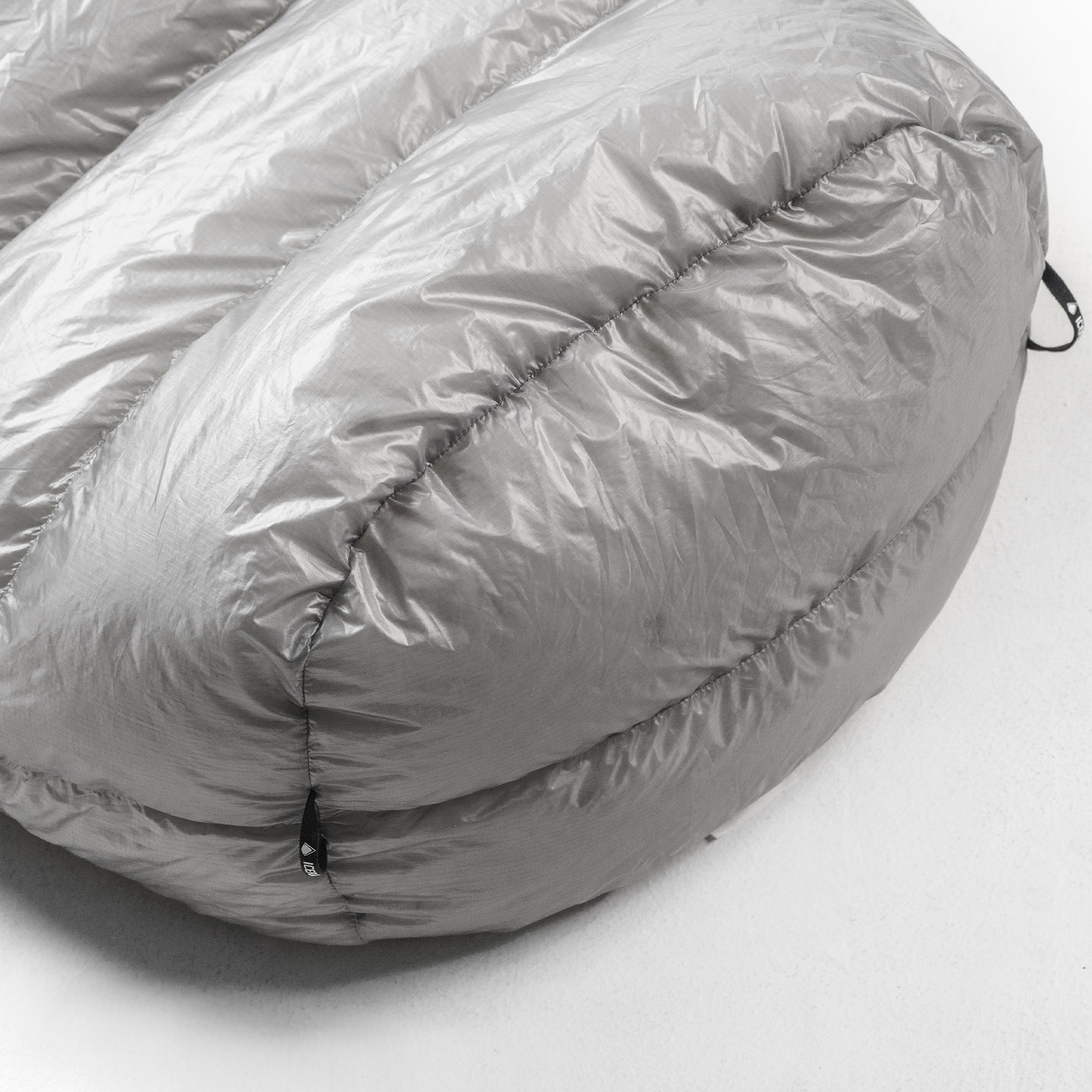 Close-up of a gray puffer jacket showing quilted, glossy fabric and stitched panels.