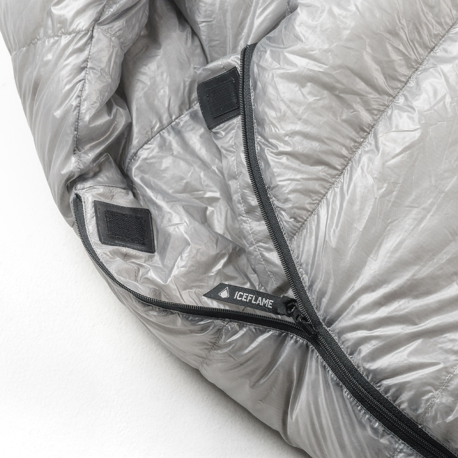 Close-up of a gray quilted jacket with a zipper, Velcro patches, and the Iceflame brand label visible at the seam area.