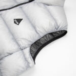 Close-up of a light gray quilted puffer jacket sleeve with a black elastic cuff and a small black triangular brand tag sewn on the fabric.