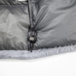 Close-up of a gray puffer jacket hem with a black drawstring toggle and stitching detail.
