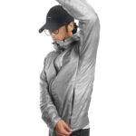 Person wearing a metallic silver puffer jacket with a raised arm, black cap, and glasses, posing to show the jacket's fit and zipper details.