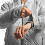 Person adjusts a sporty watch on their left wrist, wearing a silver-gray puffer jacket.